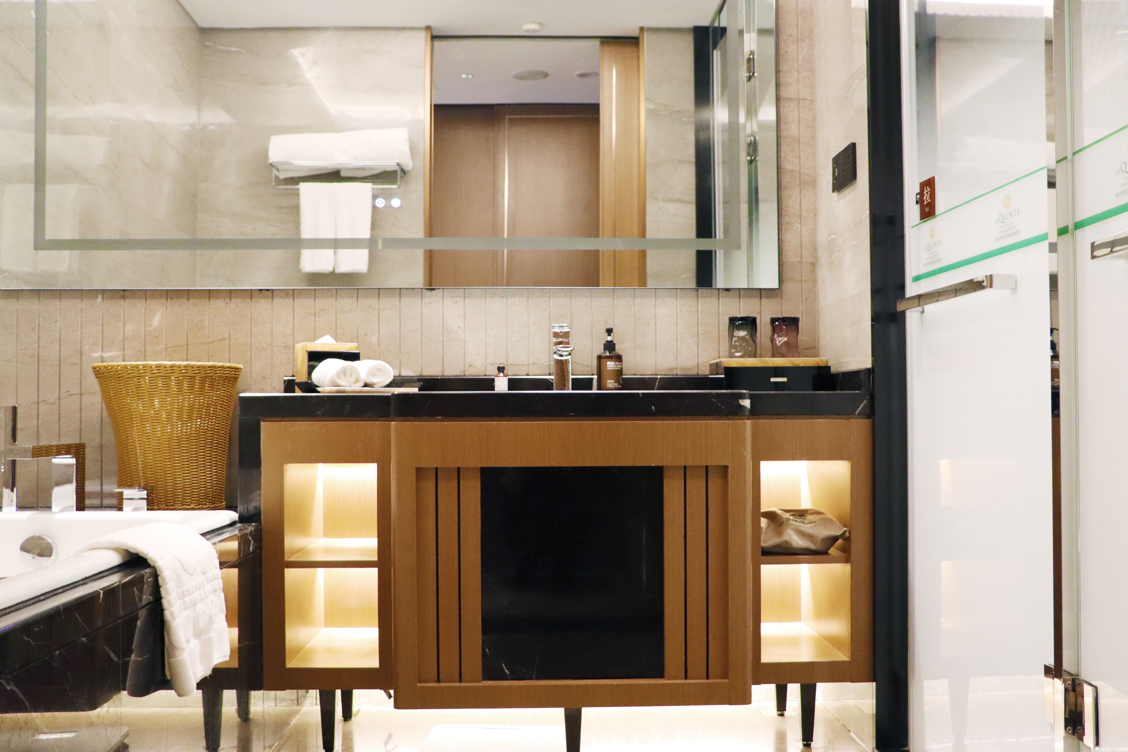 A modern bathroom with a wooden vanity, a large mirror, and a glass shower enclosure.