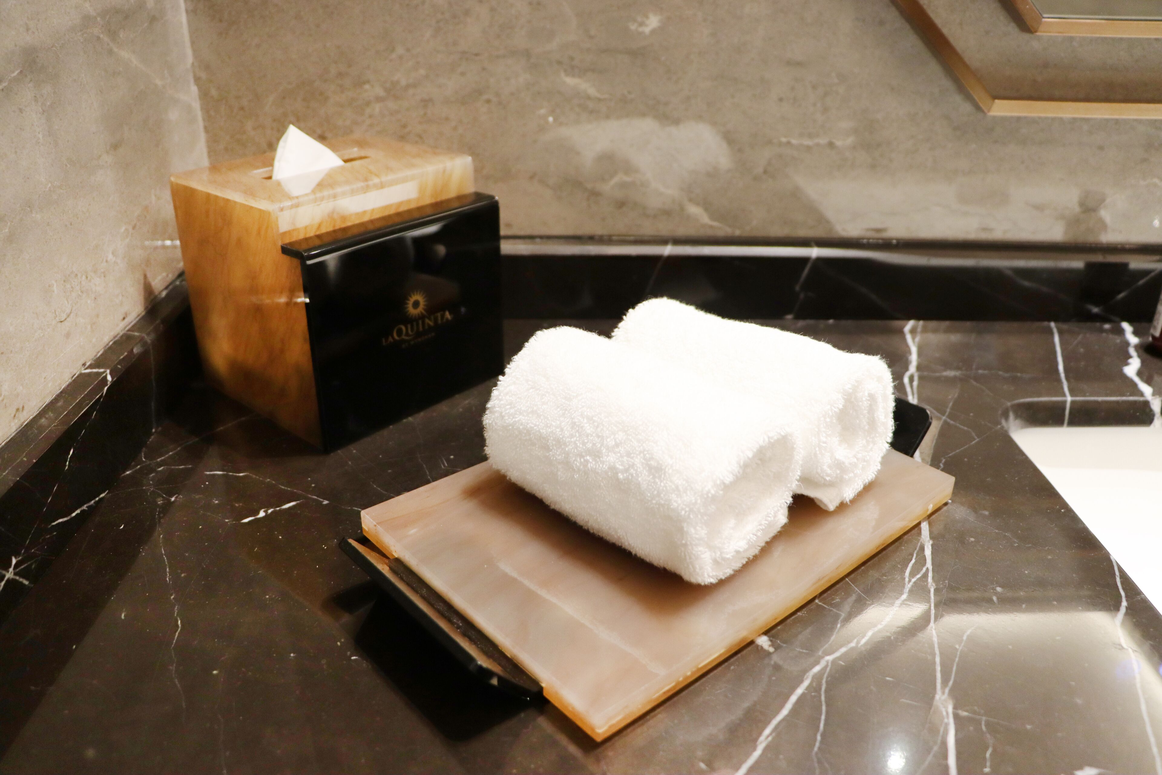 Un baño con encimera de mármol, una caja de pañuelos y una toalla blanca sobre una bandeja de madera.
