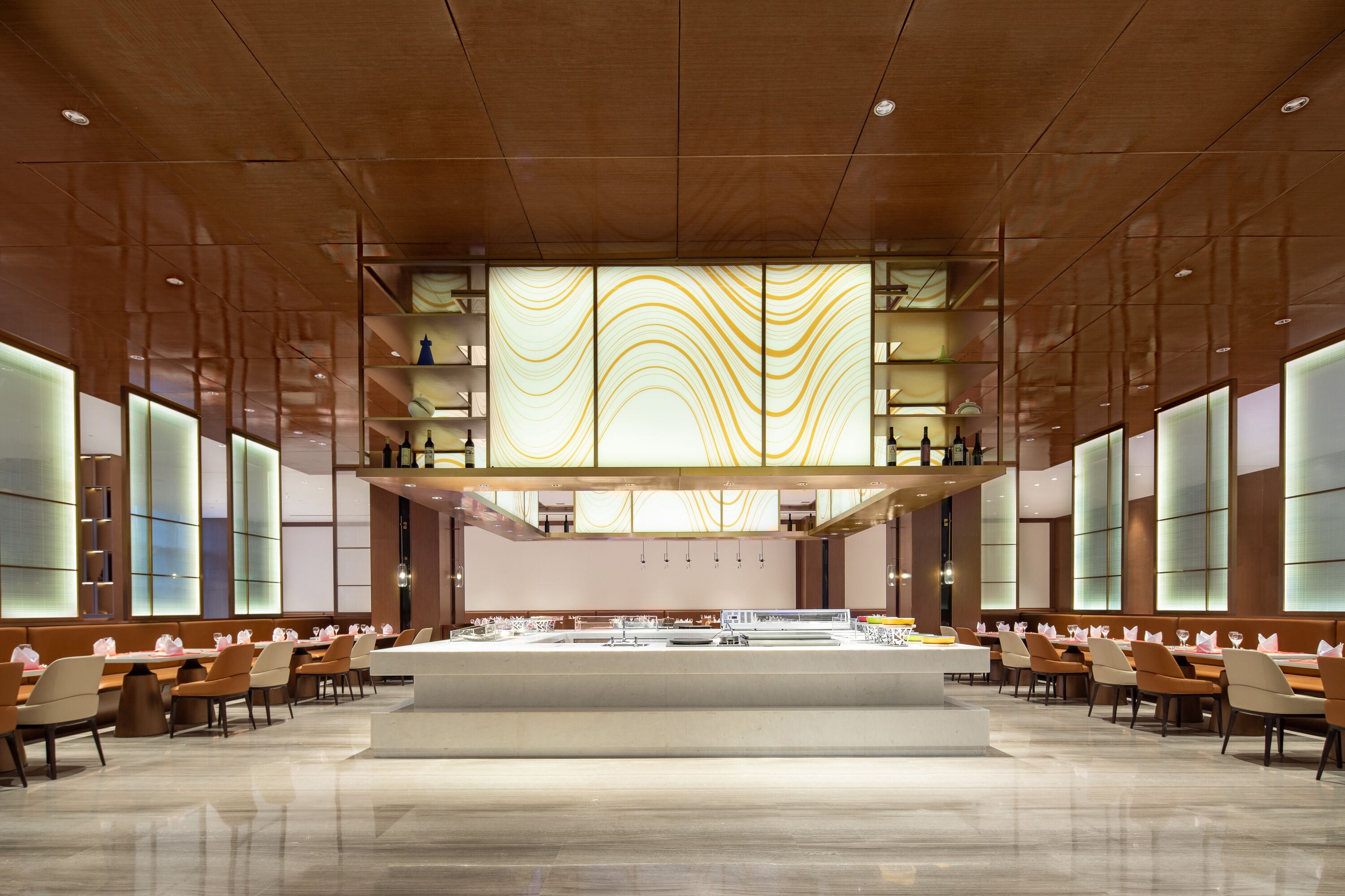 A spacious hotel lobby with a central reception area, multiple seating arrangements, and a modern design with wooden paneling and large windows.
