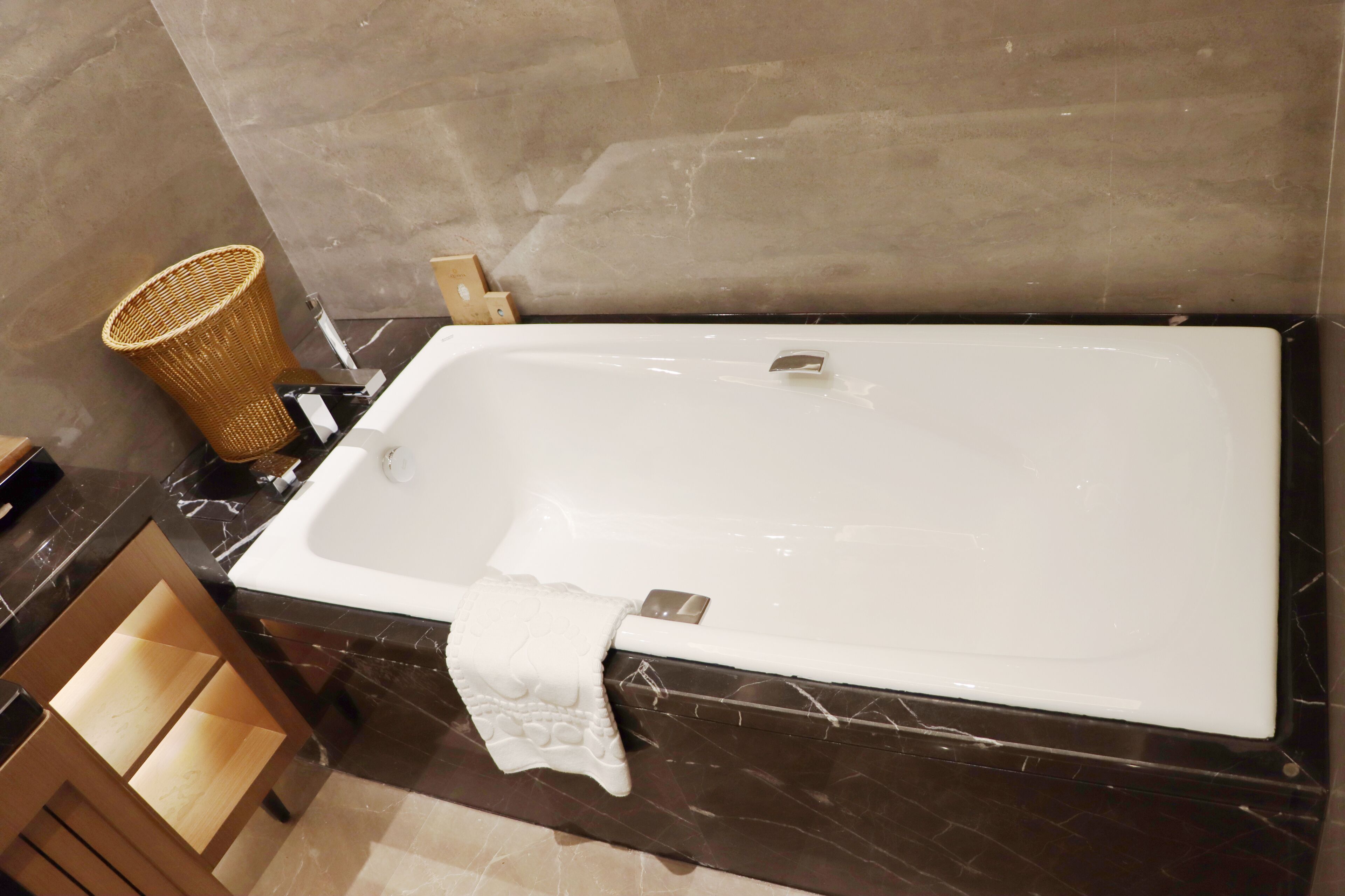 A modern bathroom with a large rectangular bathtub, a wooden vanity with open shelves, and a woven basket on the countertop.