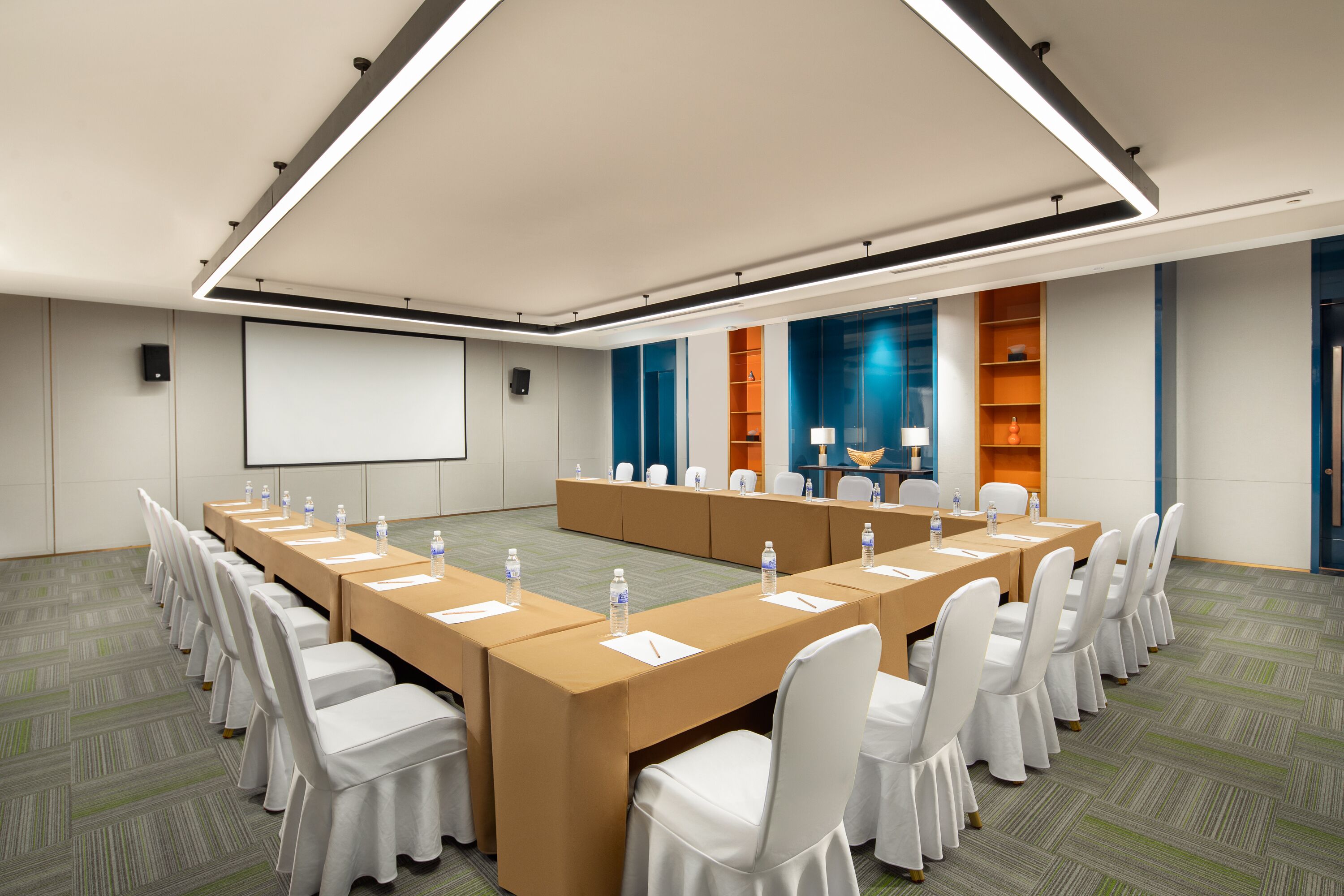 A conference room with a long table, white chairs, and a projector screen.