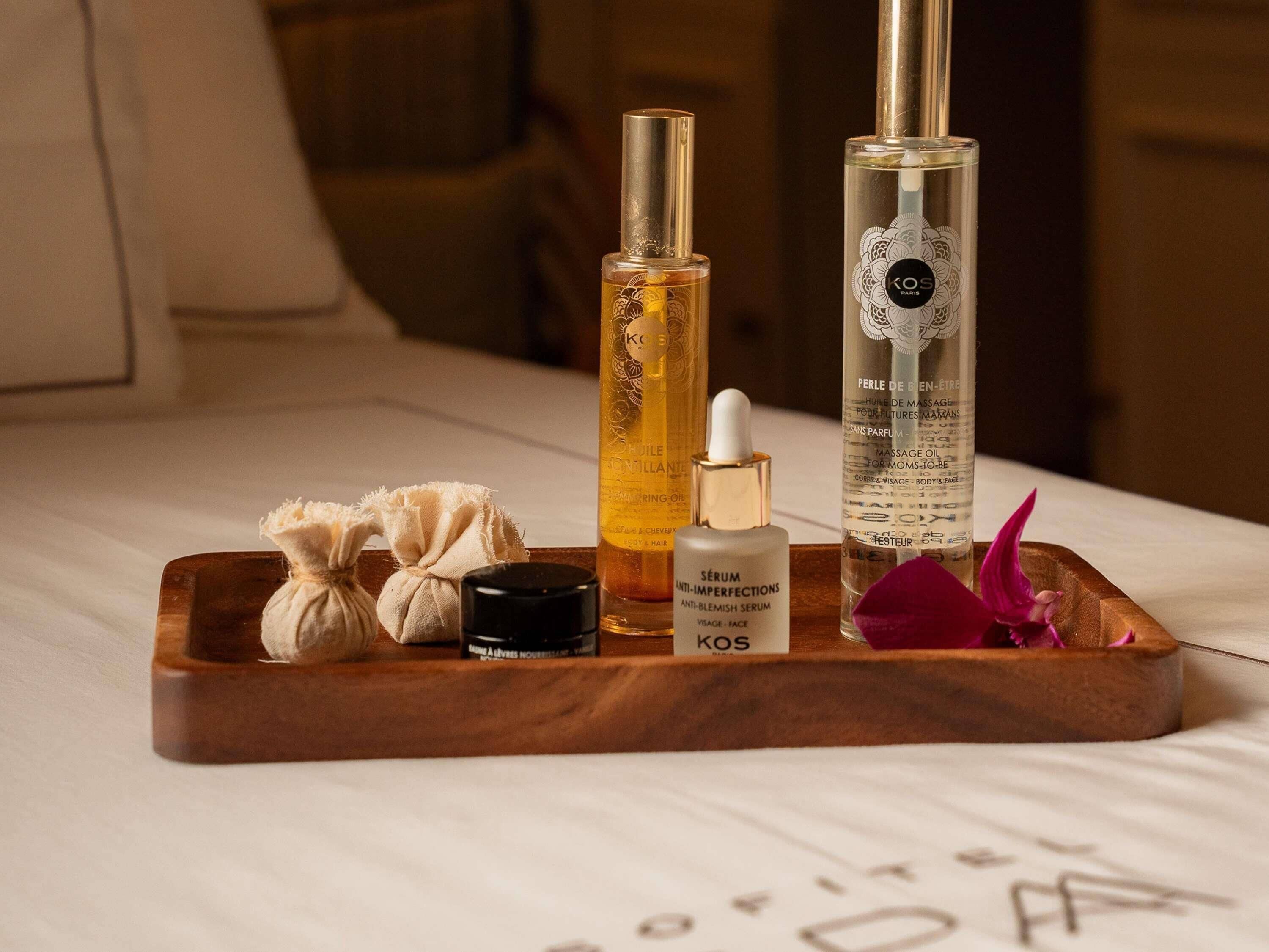 Una bandeja de madera con productos para el cuidado de la piel, un recipiente negro y una flor rosa sobre una cama.