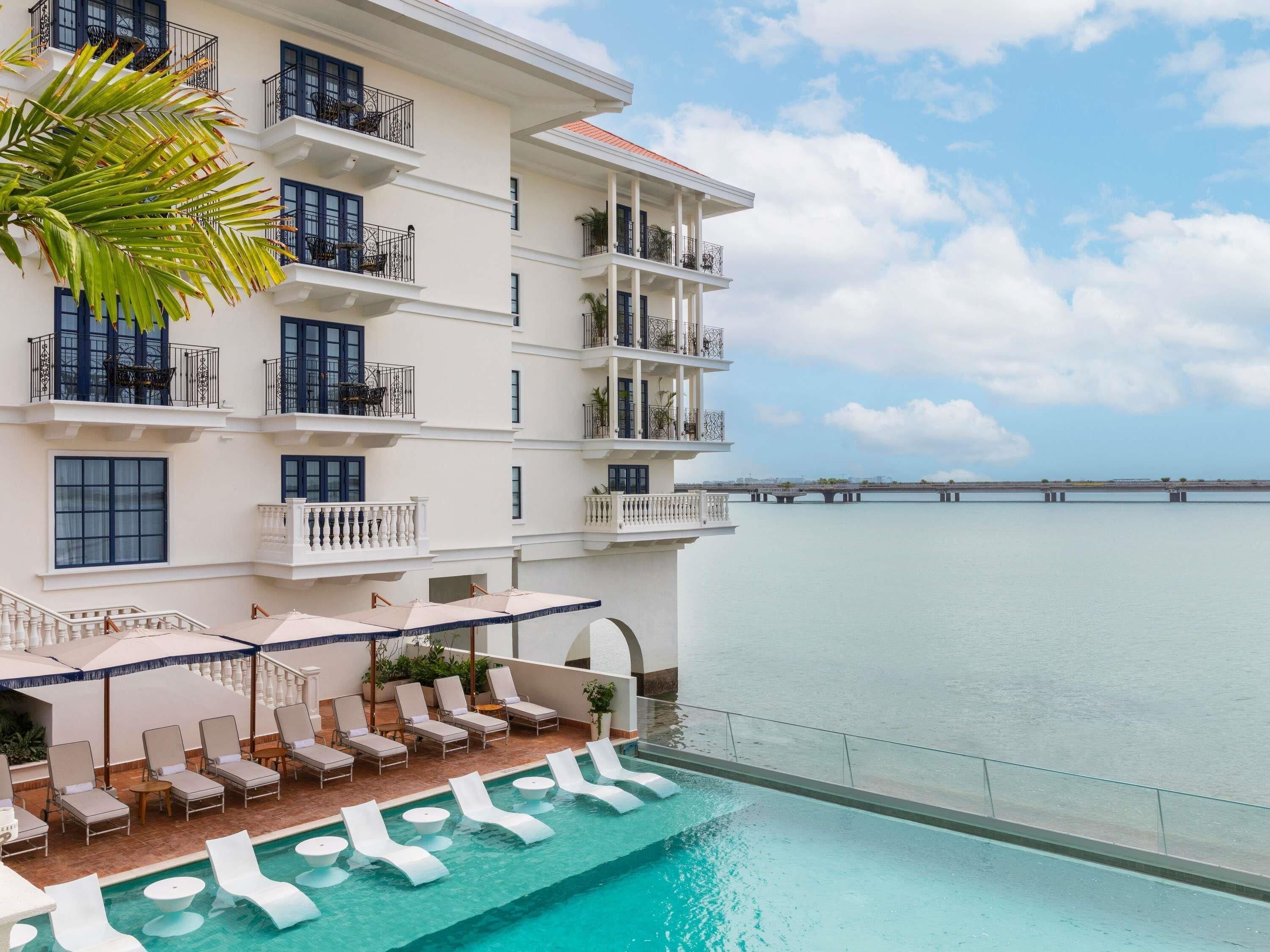 A hotel with a pool, lounge chairs, and a view of the sea.