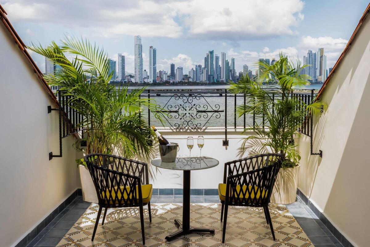 A balcony with two chairs, a table, and a view of a city skyline.