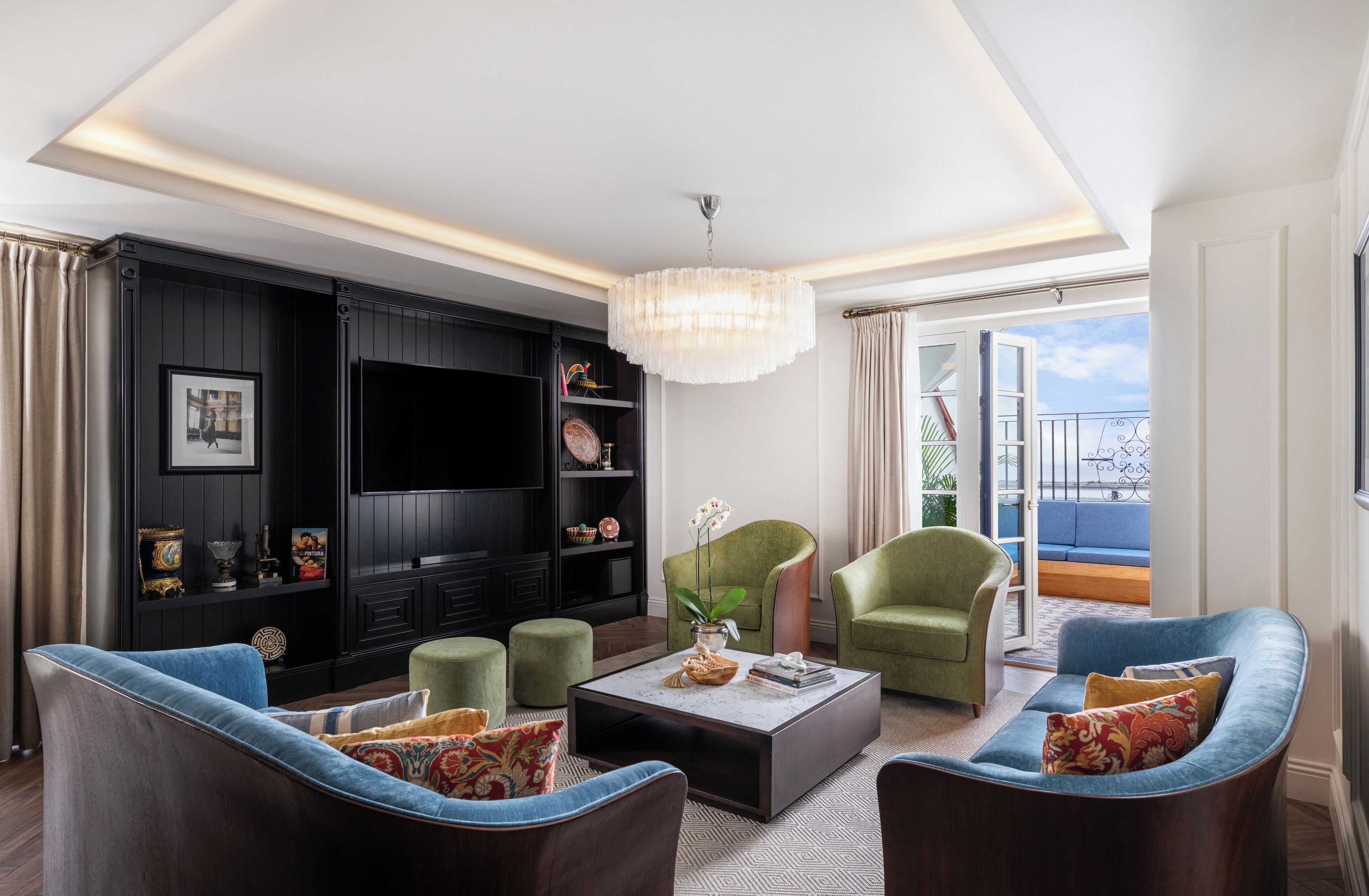 Ein modernes Wohnzimmer mit Fernseher, grünen Sesseln, einem Couchtisch und einem Balkon mit Blick.