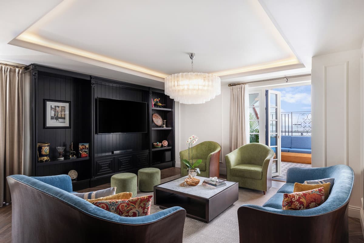 Ein modernes Wohnzimmer mit Fernseher, grünen Sesseln, einem Couchtisch und einem Balkon mit Blick.