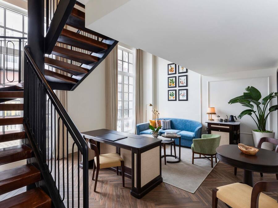 Ein modernes Wohnzimmer mit einer Holztreppe, einem blauen Sofa, einem Esstisch und einer großen Pflanze.