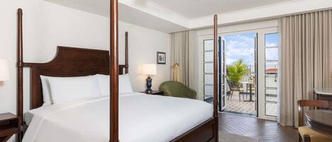 Habitación de hotel con cama con dosel, ventilador de techo, balcón con vistas y zona de comedor con mesa y sillas.