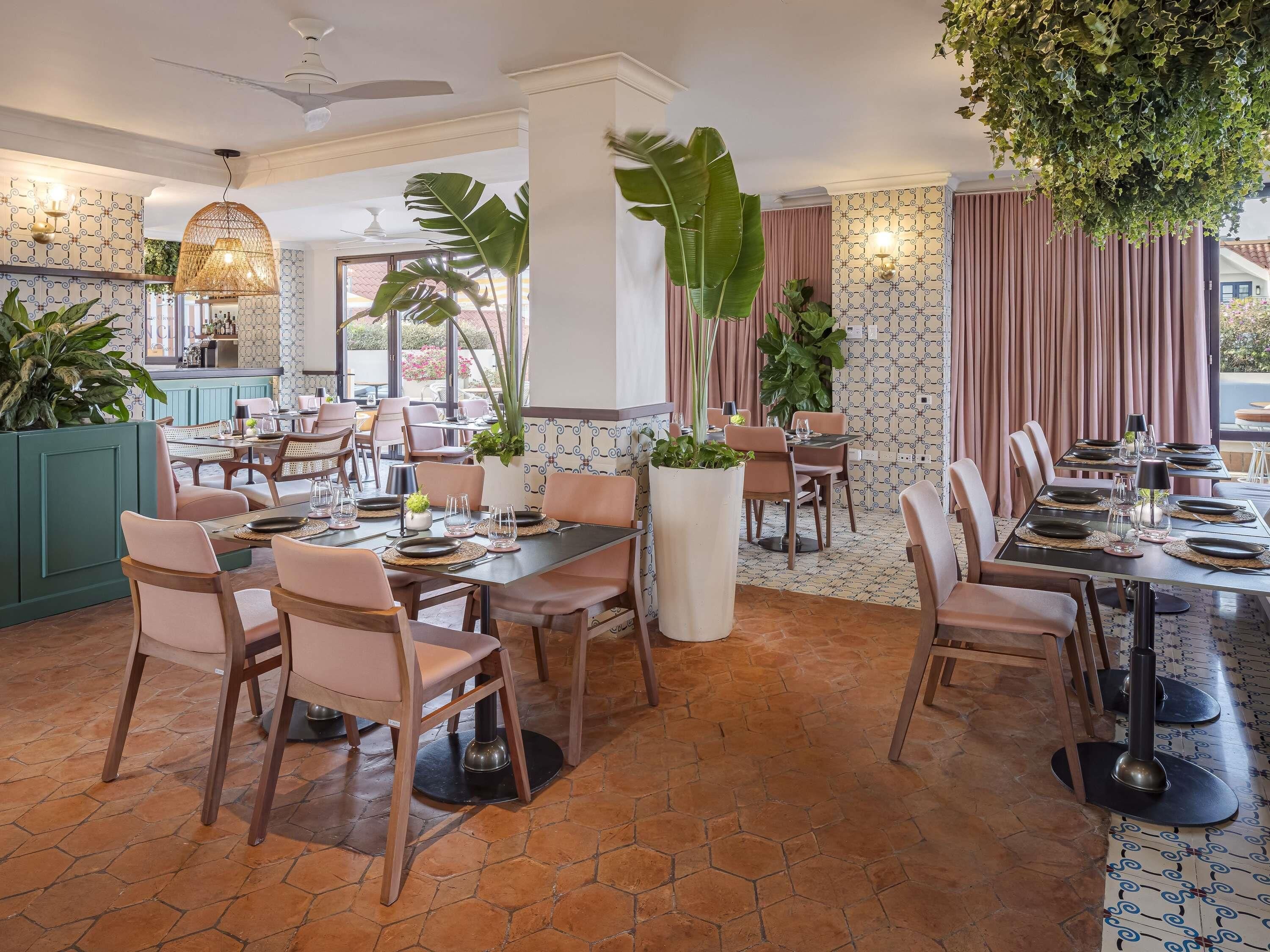 Un restaurante con varias mesas, sillas y grandes macetas con plantas.