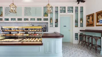 A café with a display case of pastries, a coffee machine, and a menu board listing various coffee drinks.