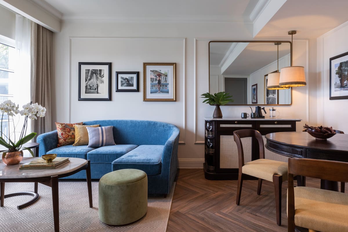 Ein modernes Wohnzimmer mit einem blauen Sofa, einem runden Couchtisch und einem Essbereich mit Holztisch und Stühlen. An der Wand hängen gerahmte Bilder und auf dem Couchtisch steht ein Topfpflanze.