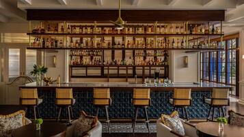 A bar area with multiple shelves of liquor bottles, wicker chairs, and a bar counter.