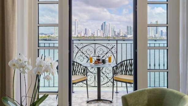 A balcony with a table, chairs, and a view of a city skyline across a body of water. - Sofitel Legend Casco Viejo, Panama City  (Panama City)