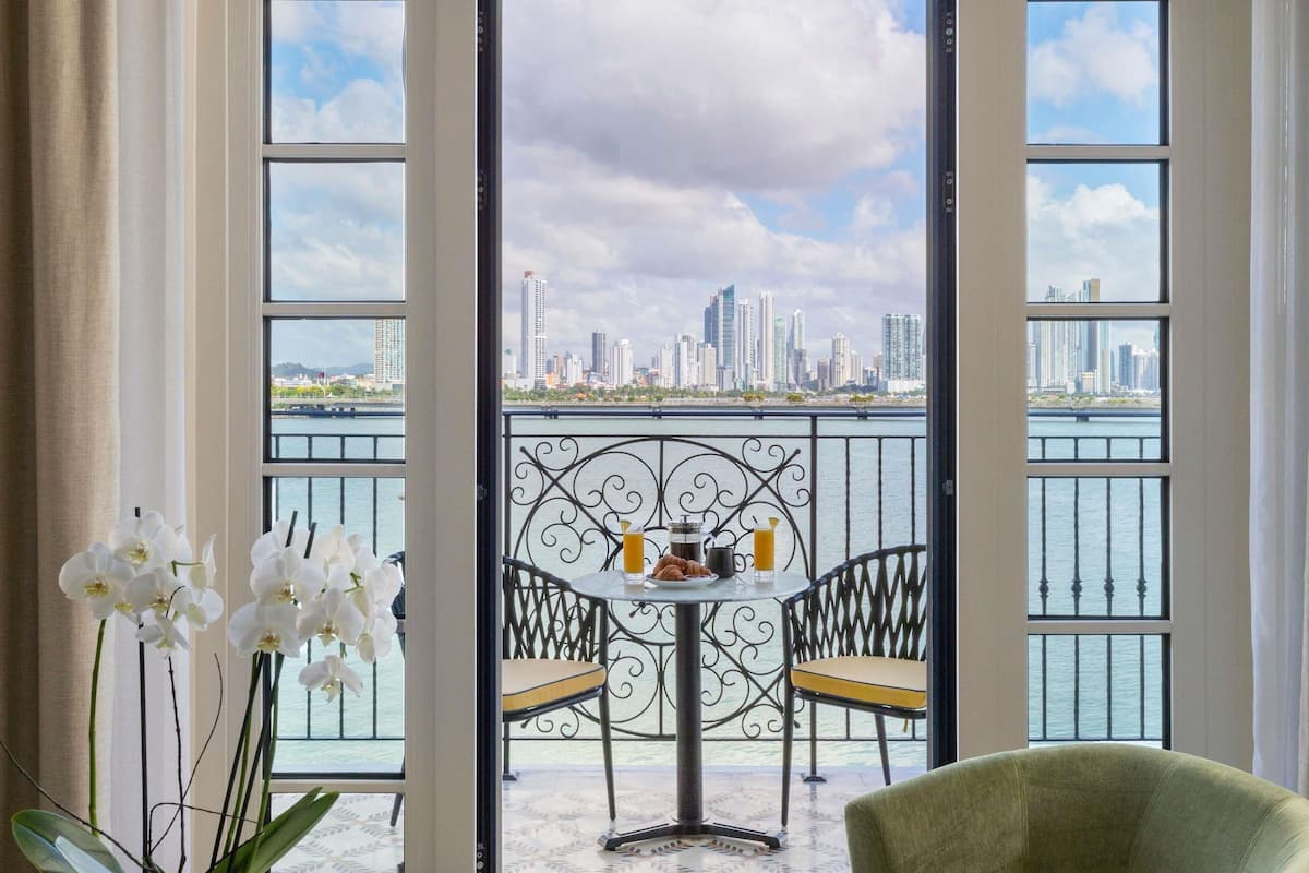 A balcony with a table, chairs, and a view of a city skyline across a body of water.