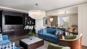 A modern living room with a large flat-screen TV, a blue sofa, a coffee table, and a chandelier.