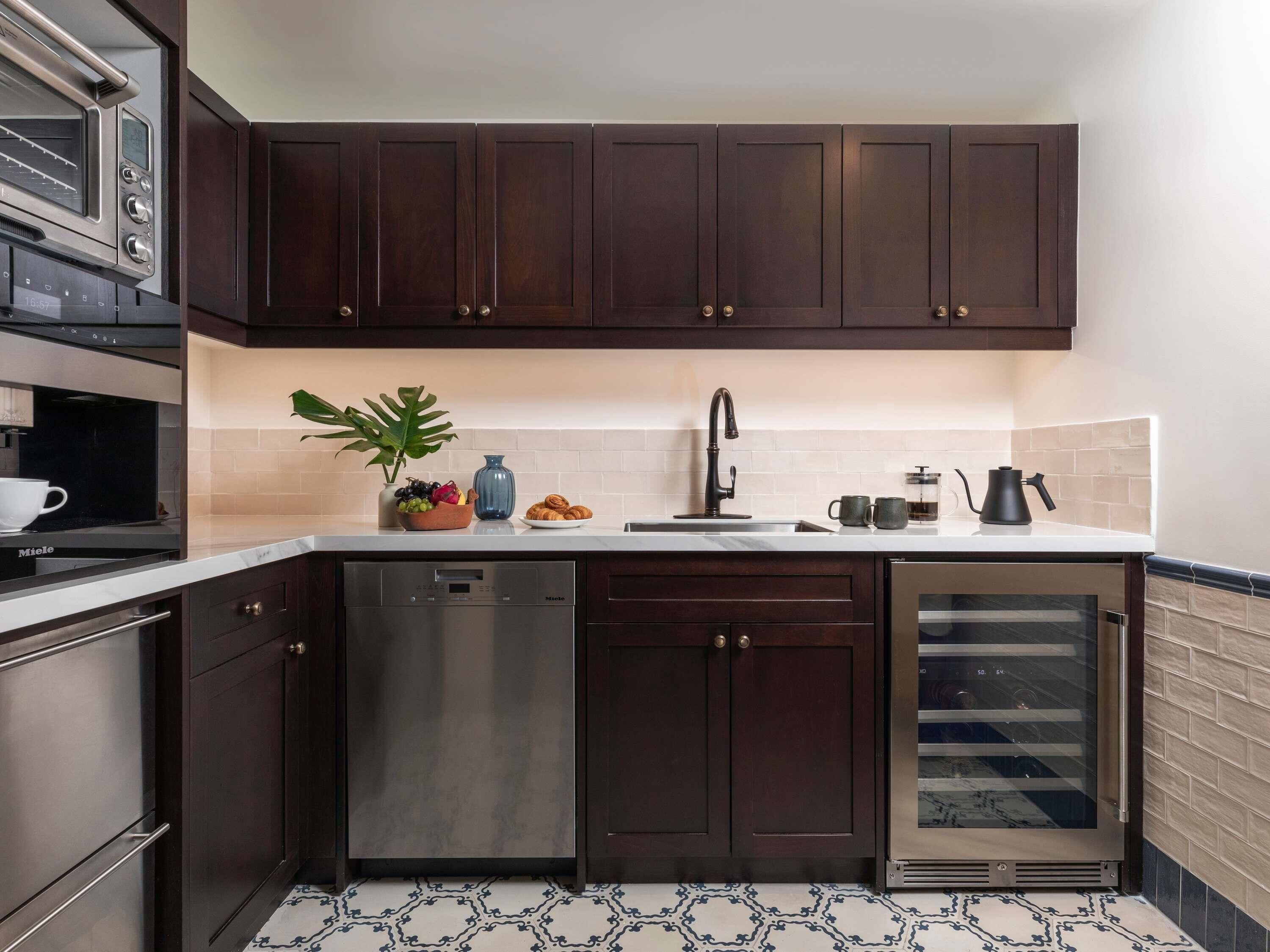 A modern kitchen with dark wood cabinets, a stainless steel dishwasher, a built-in oven, and a wine cooler.