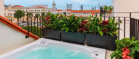 A rooftop jacuzzi with a city view, surrounded by potted plants and a balcony railing.