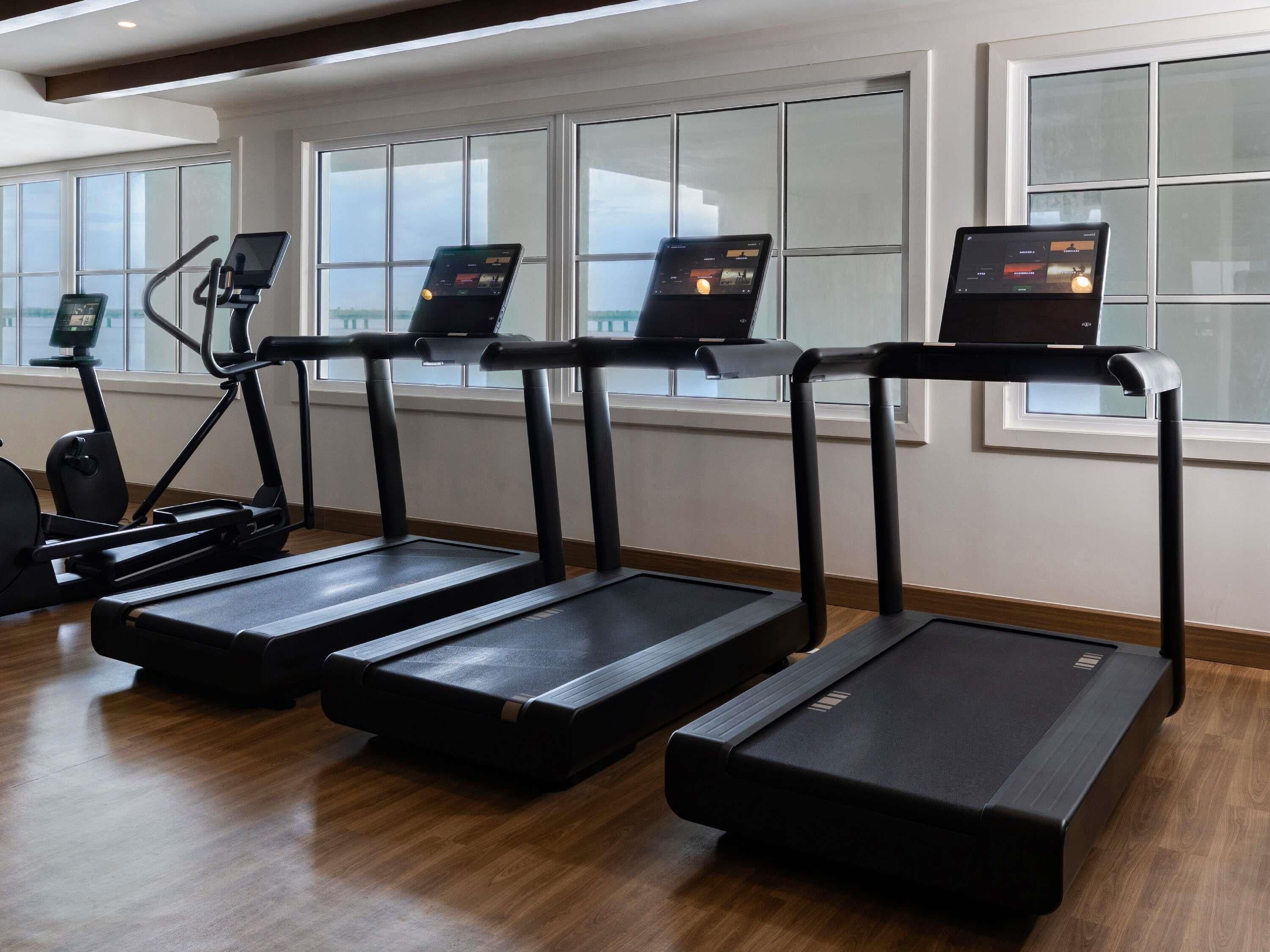 Un gimnasio con cintas de correr, bicicletas estáticas y una máquina de remo.