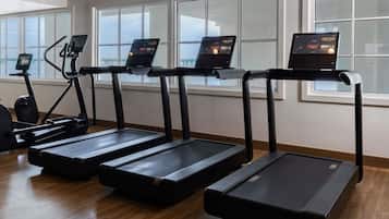 Un gimnasio con cintas de correr, bicicletas estáticas y una máquina de remo.