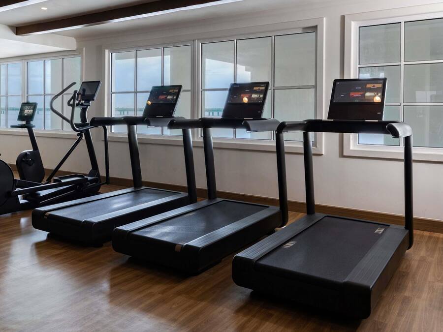 Un gimnasio con cintas de correr, bicicletas estáticas y una máquina de remo.