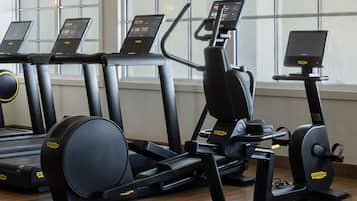 Un gimnasio con cintas de correr, elípticas y una bicicleta estática, con grandes ventanales al fondo.