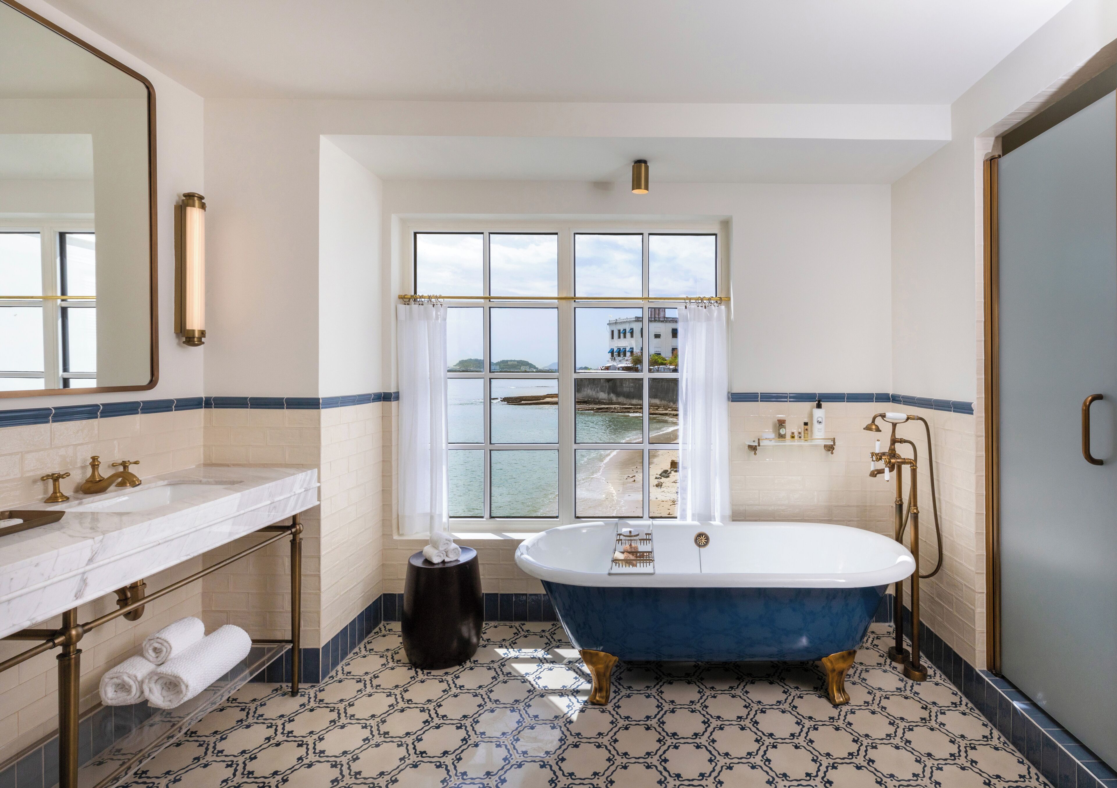 A bathroom with a large window, a bathtub, and a vanity with a mirror.