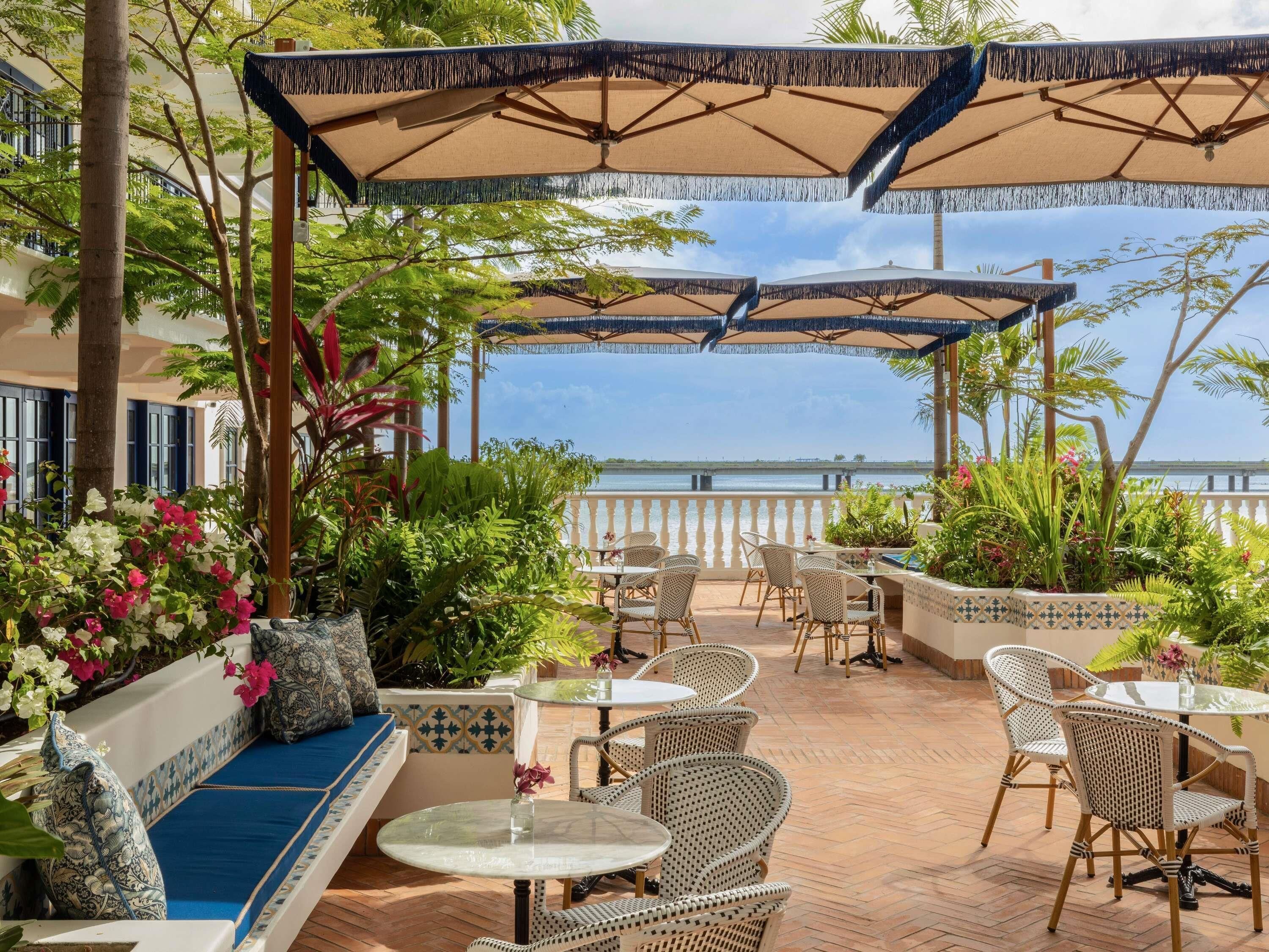 A terrace with outdoor seating, a view of the sea, and tropical plants.
