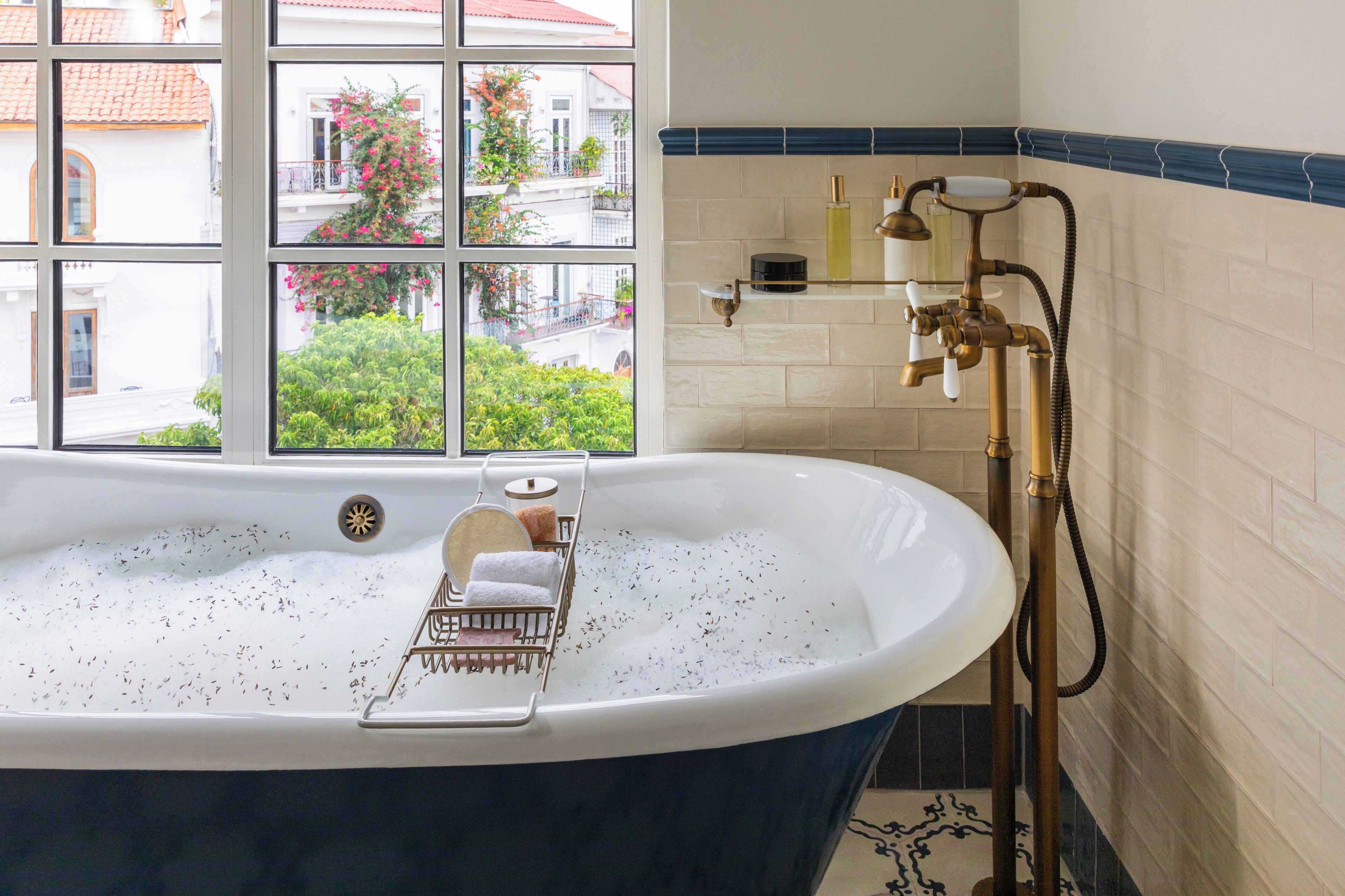 Un baño con una bañera independiente, un ventanal con vistas a edificios y follaje, y un perchero con toallas.