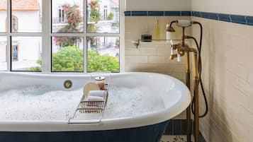 Un baño con una bañera independiente, un ventanal con vistas a edificios y follaje, y un perchero con toallas.