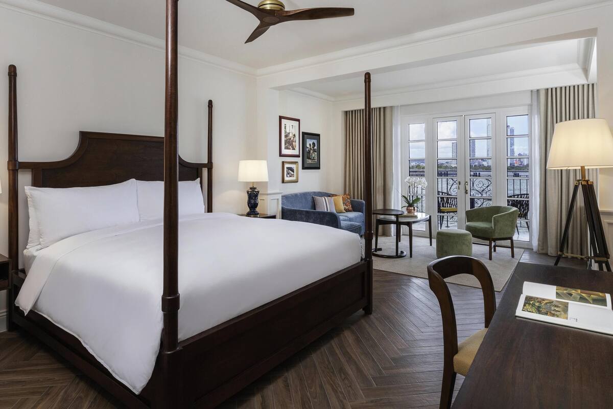 A four-poster bed with a ceiling fan, a sofa, a chair, and a table with a lamp.