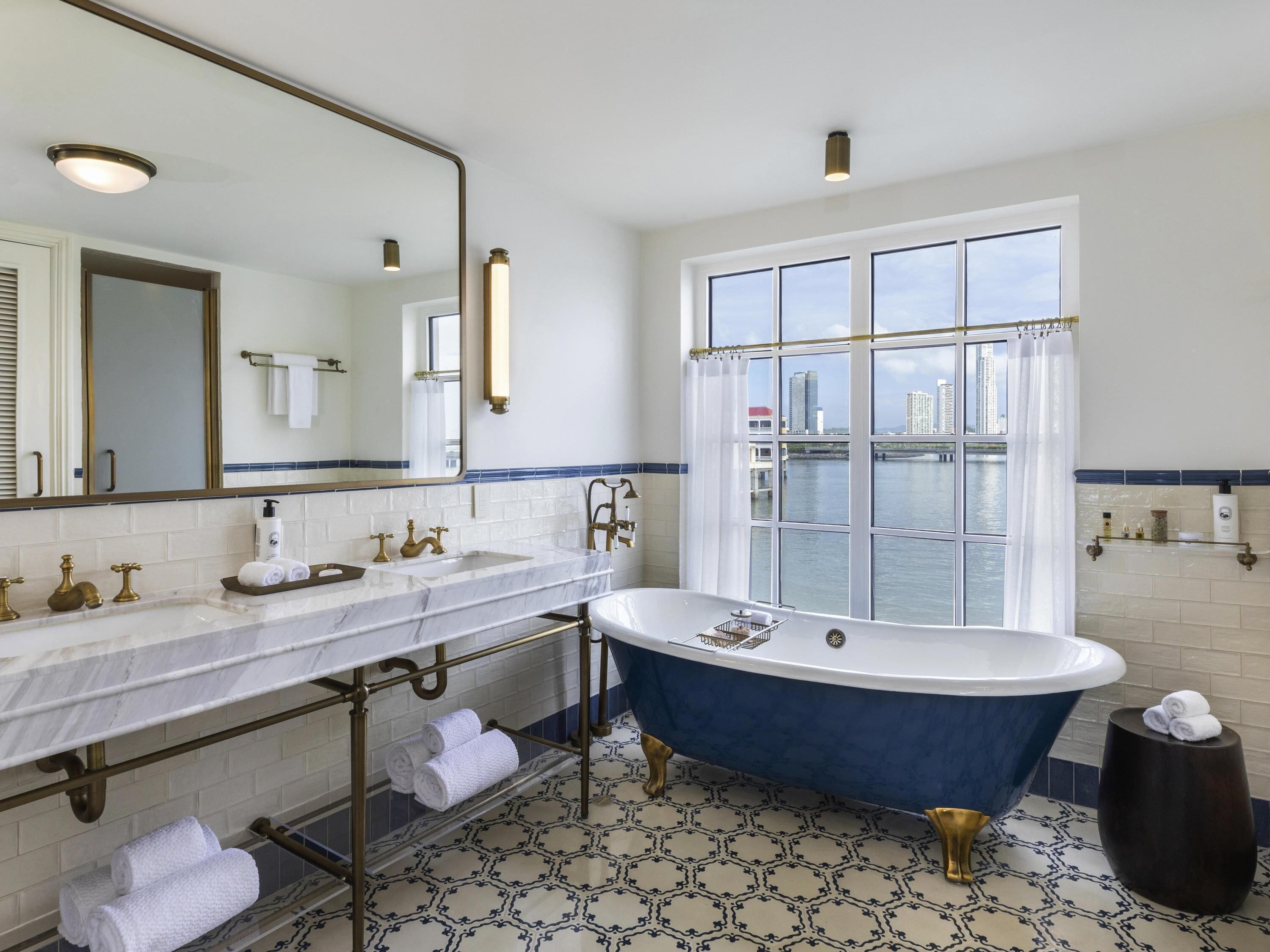 Un baño con bañera, dos lavamanos, un espejo grande y vistas de la ciudad a través de una ventana.