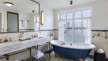 A bathroom with a bathtub, two sinks, a large mirror, and a view of a cityscape through a window.