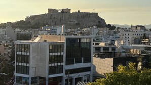 A modern building with large windows and a flat roof, located in a city with historical architecture in the background. - Park Minimal (Marousi)
