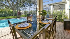 A glass-enclosed patio with a pool, outdoor furniture, and a view of the surrounding greenery.