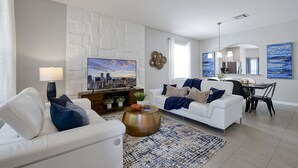 A modern living room with a white sofa, a round coffee table, and a cityscape painting.