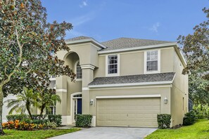 A two-story house with a beige exterior, a garage, and a well-maintained lawn. - Windsor Hills Private Pool Home ~~ 3 Miles to Disney World w/Tasteful Theming!! (Kissimmee)