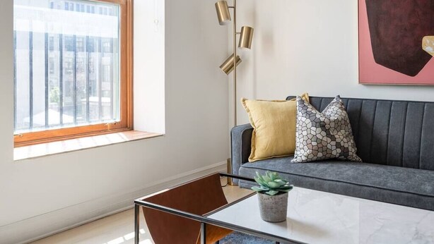 A modern living room with a grey sofa, a small table with a plant, and a floor lamp. - Modern 1 BR 1BA in center of Old Mtl | St Paul St (Montréal)