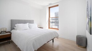 A bedroom with a large bed, a nightstand, a window with a view, and a wall-mounted radiator. - Modern 1 BR 1BA in center of Old Mtl | St Paul St (Montréal)