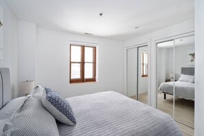 Une chambre moderne avec un grand lit, une fenêtre et une porte coulissante donnant sur une autre pièce.