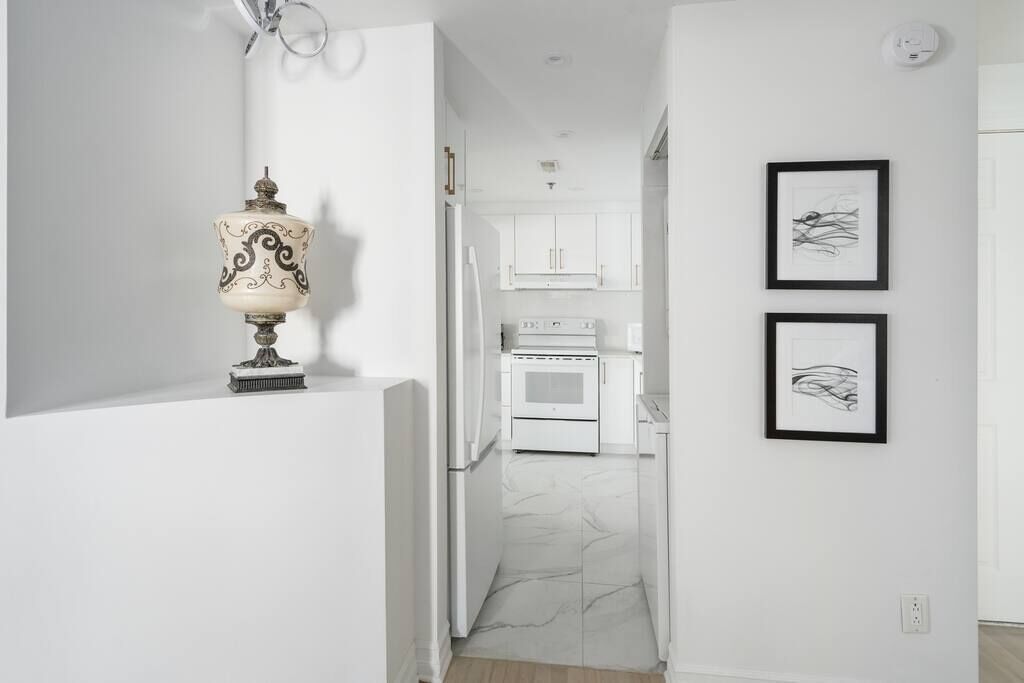 Un pasillo con piso blanco, paredes blancas, un refrigerador blanco y un horno blanco, además de dos cuadros en la pared.
