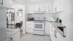 A modern kitchen with white cabinetry, a built-in oven, a microwave, and a coffee maker. - Sublime 3BR 2BA Apt | Old Mtl | St Paul ST | (Montréal)