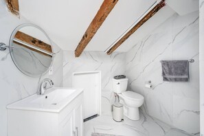 Une salle de bain moderne avec un lavabo en marbre blanc, un miroir rond, des toilettes et un porte-serviettes.