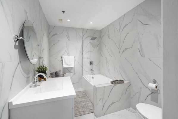 Et moderne badeværelse med en marmorvæg, et fristående badekar, en vask og et toilet.