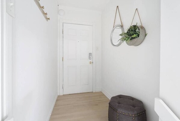 A hallway with a white door, a small stool, and two hanging planters with greenery.