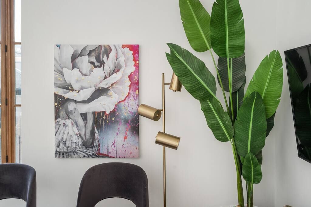 Une pièce avec un grand tableau abstrait, une plante haute et un lampadaire.