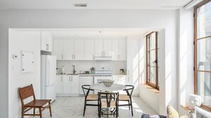 A modern kitchen with white cabinets, a dining table with chairs, and a window providing natural light. - Chic & Modern 3B 1B Apt | Old Mtl | St Paul St | (Montréal)