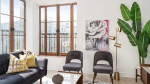 A modern living room with a black sofa, two grey chairs, a coffee table, a large abstract painting, a tall floor lamp, and a large green plant. - Chic & Modern 3B 1B Apt | Old Mtl | St Paul St | (Montréal)