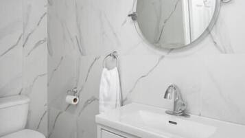 Un baño con inodoro blanco, lavamanos con espejo arriba y paredes con diseño de mármol.