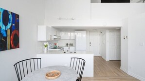 Une cuisine moderne avec des meubles blancs, un îlot en marbre et un coin repas comprenant une table ronde et des chaises.