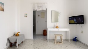 Una habitación con un escritorio blanco, un televisor montado en la pared, un taburete pequeño y una puerta que da a otra habitación.